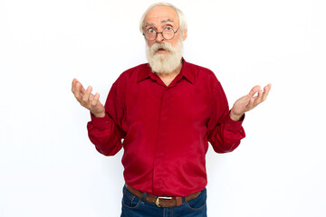 Confused senior man shrugging. Surprised Caucasian male model with gray hair and beard in red shirt and glasses looking at camera with raised hands, showing helpless gesture. Confusion, choice concept