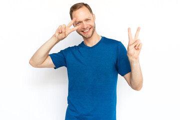 Happy Caucasian man showing peace sign at camera. Bearded man in T-shirt looking at camera, smiling and standing on white background. Satisfaction, achievement, winning concept