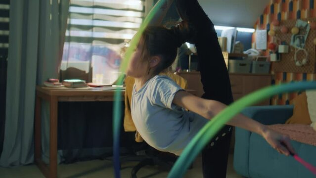Young asian girl dances with gymnastic ribbon, showing vertical leg-split and spins around herself. Gymnastics training. Sports hobby. Upgrading physical health on quarantine. Slow motion.