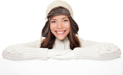 Winter woman sign banner. Cute smiling woman in warm winter sweater and wool cap showing blank white paper poster isolated cutout PNG on transparent background.
