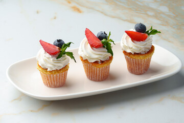 Cupcakes with strawberries and cream on white table