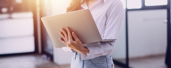 Woman hand using smart phone and laptop in outdoor nature park and sunset sky with bokeh light abstract background. Technology business and freelance working concept. Vintage tone filter color style.