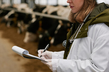 Close-up of female veterinarian in white coat making notes in card after medical exam of animals