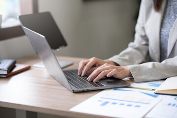Close-up businesswomen using laptop computers to work attentively on a table with various documents such as charts and graphs of important financial data.
