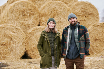 Portrait of couple of farmers smiling at camera standing outdoors with haystack in the background