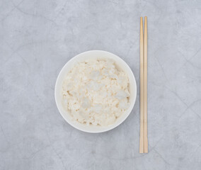 Cooked white rice in white bowl with wood sticks on grey background. Selective focus. Asian food concept