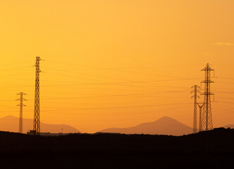 Calima, sand storm in Lanzarote. View of Volcanoes and electricity transmission pylons silhouetted against orange sky. Costa Teguise, Canary Islands, Spain.