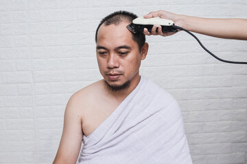 Muslim man wearing white ihram clothes doing Tahallul, shaving their head after performing tawaf...