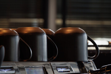 Black color ceramic coffee cup warming on top of espresso coffee maker machine. Preparing coffee cup temperature before brewing.