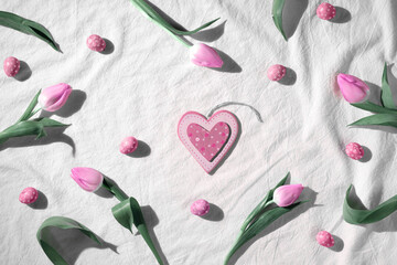 Easter background, pink tulip flowers and quail eggs. Decorated background around wooden heart...