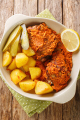 Galinha a africana African chicken Style of Macau served with potatoes, lemon and pickle close up on the pot on the table. Vertical top view from above