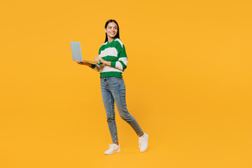Full body young latin IT woman wears casual green knitted sweater hold use work on laptop pc computer look aside on area isolated on plain yellow background studio portrait People lifestyle concept.