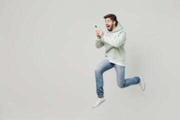 Full body side view overjoyed excited fun young caucasian man wear mint hoody jump high use mobile...