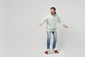Full body side profile view fun young excited amazed happy smilign caucasian man wearing mint hoody riding skateboard isolated on plain solid white background studio portrait People lifestyle concept