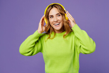 Young happy woman 30s wearing casual green knitted sweater headphones listening to music dance look...