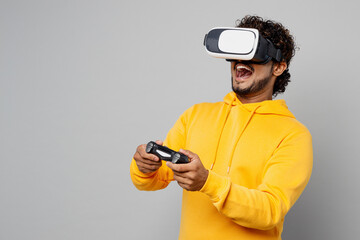 Young Indian man 20s he wearing casual yellow hoody hold in hand play pc game with joystick console...