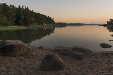 Nagu, Finland - 12.06.2022: The quiet shore of the bay after sunset. A line of trees on the horizon. Sandy beach with rocks in the foreground. Nature of Finland.
