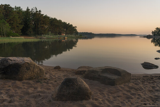 Nagu, Finland - 12.06.2022: The quiet shore of the bay after sunset. A line of trees on the horizon. Sandy beach with rocks in the foreground. Nature of Finland.