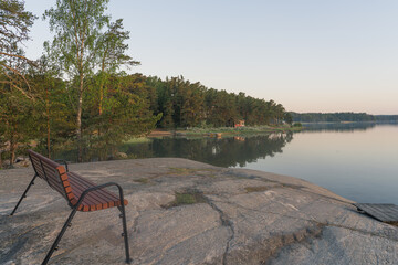 Nagu, Finland - 12.06.2022: Evening Bay. Rocky shore with pine trees and a bench in the foreground. Nature of Finland. Scandinavia.