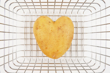 At the bottom of the supermarket basket is a potato tuber in the shape of a heart on a white background.The concept of healthy dietary nutrition, wholesale and retail sale or purchase of potatoes.