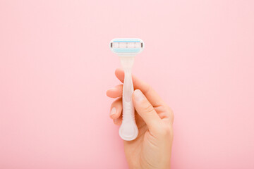 Young adult woman hand holding razor on light pink table background. Pastel color. Closeup. Female...