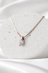 Golden necklace with crystals on concrete podium on white silk background, rose gold, single...