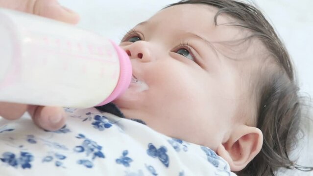 Cute baby girl have fun drinking milk from bottle that mother feed her.