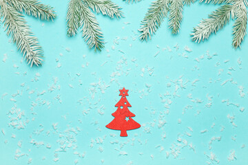 Snow-covered fir branches, a wooden red Christmas tree and artificial snow lying on a blue background. The concept of Christmas and New Year.