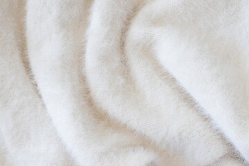 Soft beige knitted fabric as background, closeup. Fluffy light sweater or scarf gathered in waves....