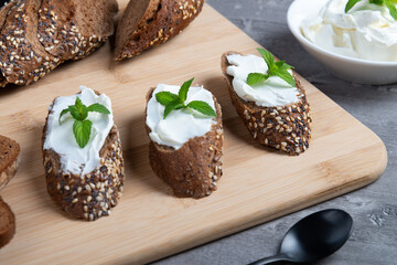 Home made bread on a wooden cutting board with curd cheese and ricotta and herbs. Decorated with...