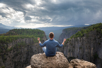 The man meditates in the lotus position on top of a mountain