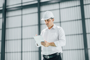 warehouse manager with tablet and ..radio communication his worker working in background in...