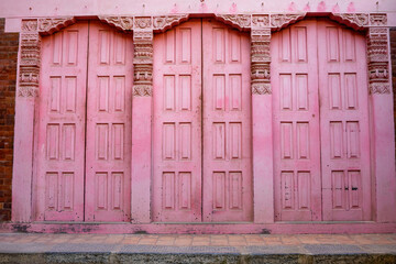 Frontal view of a pink traditional wooden house facade in a small village in Nepal. Three large closed wooden doors