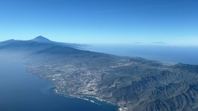 Aerial view from a jet cockpit of Tenerife Island, Santa Cruz city and the Teide volcano, in a splendid winter moorning, with a deep blue sky. Canary Islands. Spain. 4k