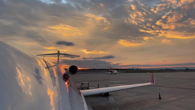 Upper jet  fuselage view just before sunset with a beautiful winter sky with the sky reflected in the plane, and another plane taxing.