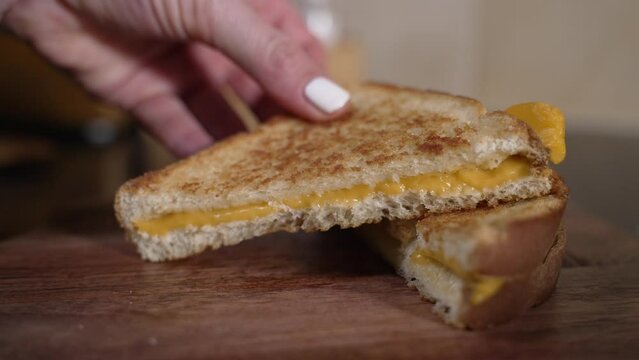 Woman places sliced grilled cheese sandwhich on cutting board