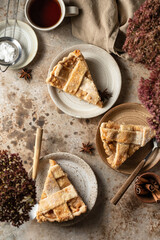 Three servings of american apple pie with cutlery and tea, top view table scene on brown textured background