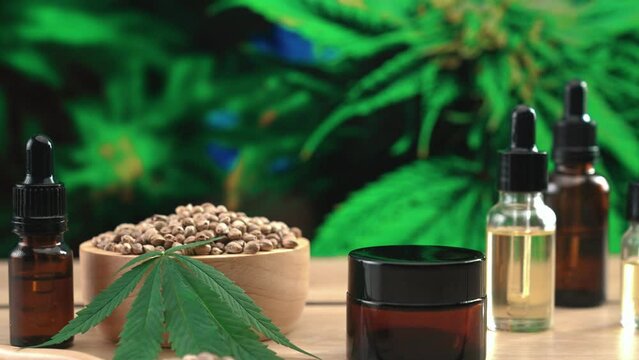Natural skincare cosmetic mockup product produced in cannabis legalized laboratory. CBD oil, hemp seed, and moisturizing cream jar product on table with garden of cannabis plants background. Copyspace
