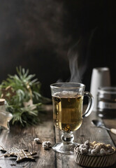 A glass of green tea with steaming and Christmas decoration on wooden table. Dark moody, Winter time. Text space