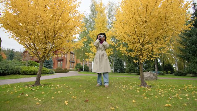 Picturesque landscape with colorful, autumn foliage and lush, green lawns. Female photographer enjoying scenic views of natural environment in city suburbs. High quality 4k footage