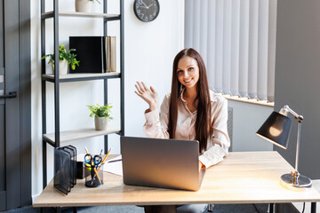Happy executive woman greeting on videocall on laptop sitting on her desk at office