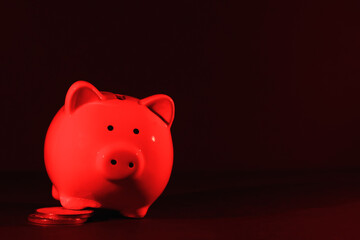 Piggy bank with coins on a dark background with red backlight, copy space. Banking concept. Bright neon lights
