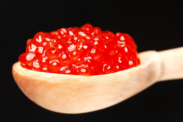 Delicious red caviar in wooden spoon on black background