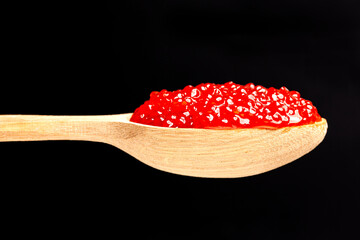 Delicious red caviar in wooden spoon on black background