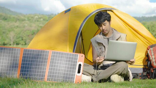 4K Young travel man relax and enjoy camping . Hand male plug in portable solar panel charging laptop computer by multipurpose cable, Clean energy for using in camping or at home when NO electricity