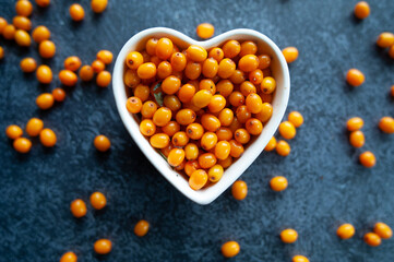 Sea buckthorn berries in a heart shaped bowl, orange healthy berries, macro. Rustic style, top view