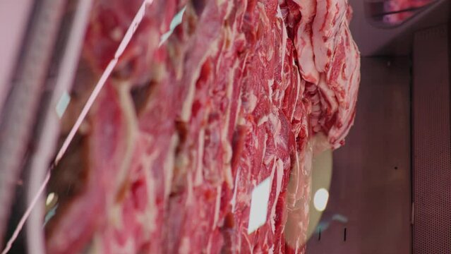 Vertical Screen: Zoom out raw lamb meat chops and loin in window showcase for sale. Layout of lamb meat in meat department in butchers shop.