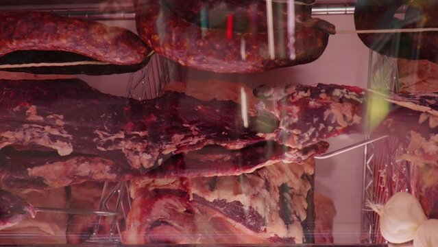 Vertical Screen: Slices of dried or smoked beef meat along with types of sausages in dry ading cabinet. Dry-aged cuts of raw meat. Food manufactoring.