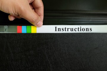 Hand picking instructions file record in black binder folder. Work instruction concept.