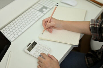 Top view, A female accountant taking notes on her notebook, using calculator